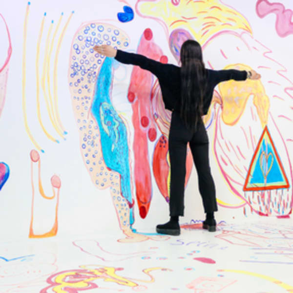 a student stands in front of coloruful artwork with her arms splayed