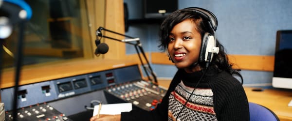 Woman in a radio booth with headphones on and a multicoloured jumper