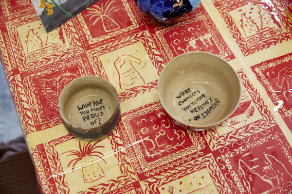 Two bowls lit on a patterned table, which read' what are you most proud of?' and 'what connects you to your heritage or identity?'