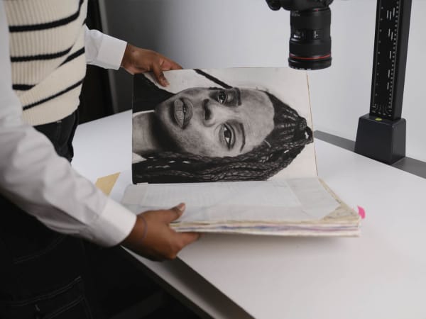 Close up of student taking a photograph on the stand of their work. In shot is a portrait of the student created in charcoal.