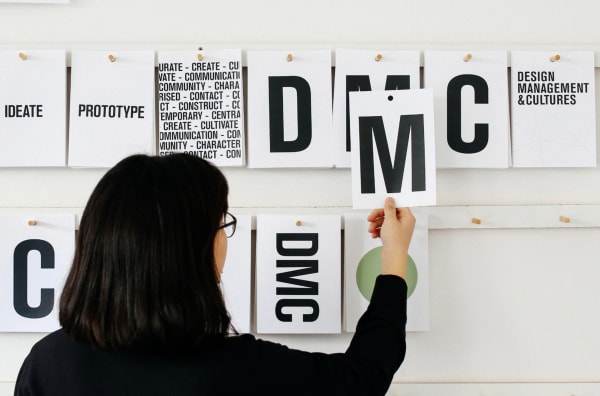 person picking up poster with letter M printed.