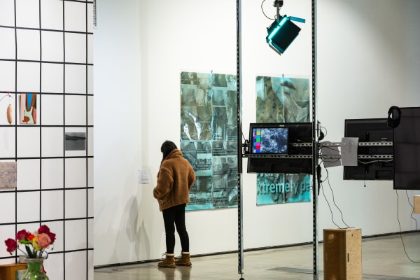 A wide shot of the Lethaby gallery with people viewing an installation. Panels, screens and posters are visible and a grid structure to the left.