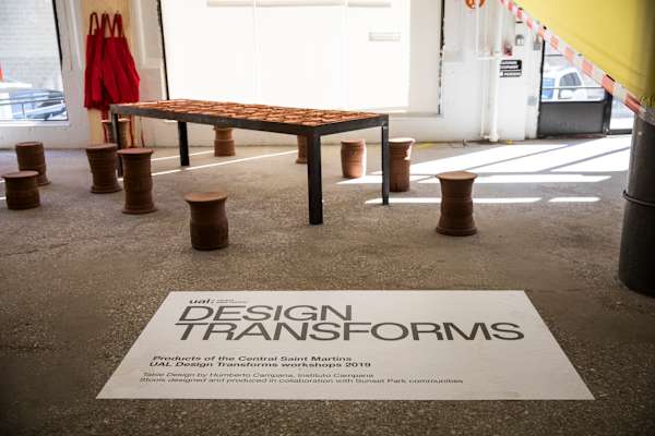 A floor-level shot of clay stools and bench in an industrial setting, next to a white floor poster panel with the heading 'Design Transforms' and the CSM logo and subtext indicating that the designs are from student workshops in 2019.