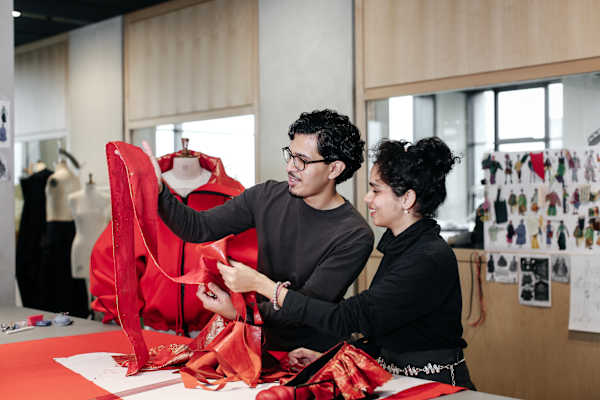 One South Asian male and one South Asian female in a workshop holding red fabric materials at a table