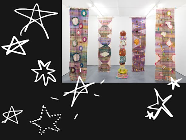 Giant multi-coloured, textured textile banners hanging from the ceiling in a white room, around a central totem-pole-like artwork on the floor 