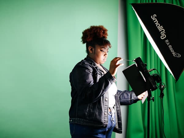 Student adjusting lighting equipment in a green screen studio.