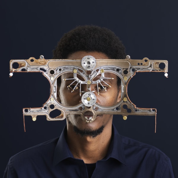 A portrait photo of a man of African descent looking into the camera, wearing oversized, futuristic glasses made out of metal