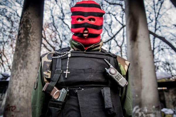 Person in a red and black striped balaclava and bulletproof vest