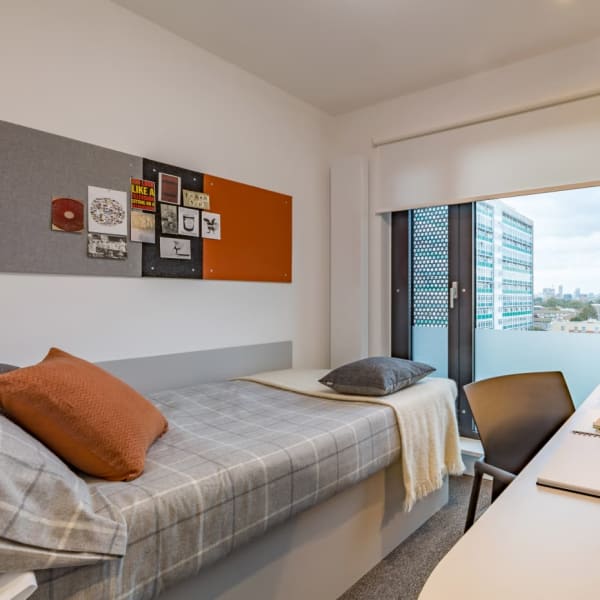 view of a single bedroom showing light room , signle bed facing a large window with a view of the other buildings and a desk space