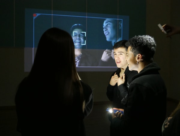 photograph of three students in a dark room with projection of their faces
