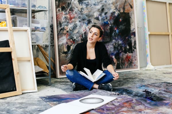 Woman sat on floor surrounded by artwork in the studio