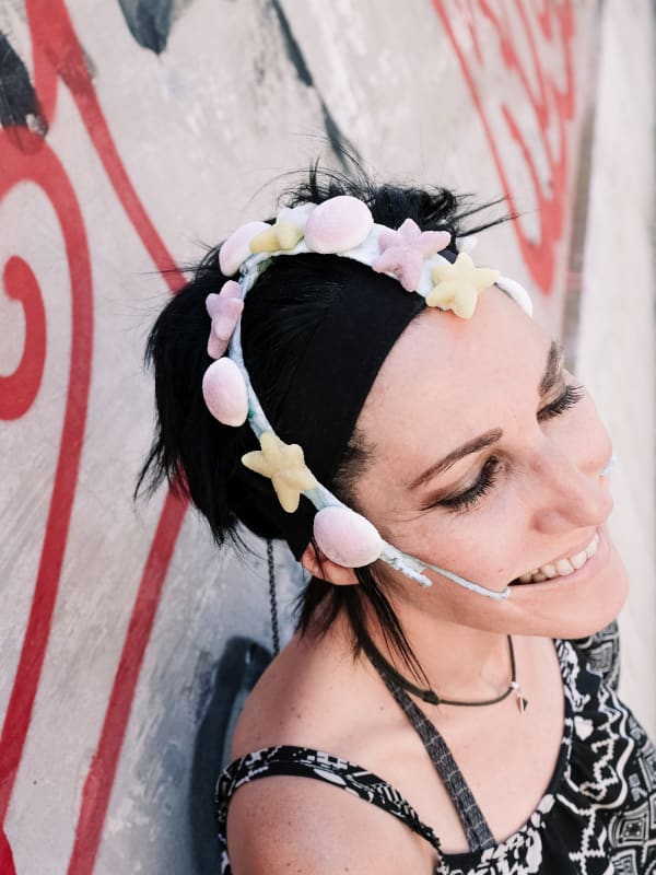 A woman smiling with a headpiece on covered in bright shapes. 