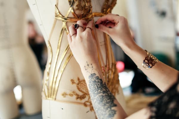 Student working on a gold bodice on a mannequin.
