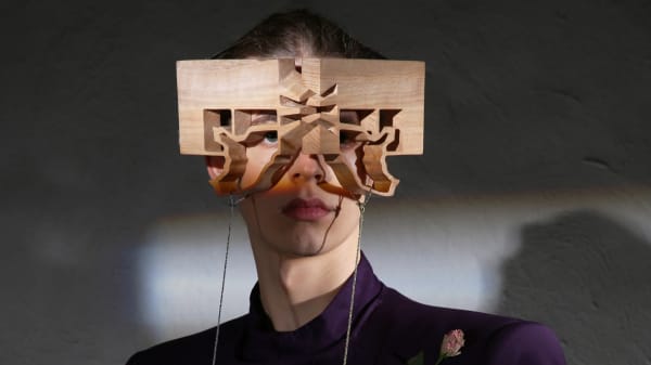 Butterfly-shaped wooden eyewear modeled by male in purple suit.