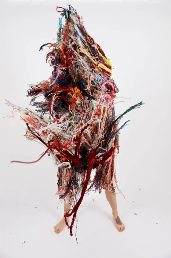 A person wearing a costume made entirely from strands of coloured wool