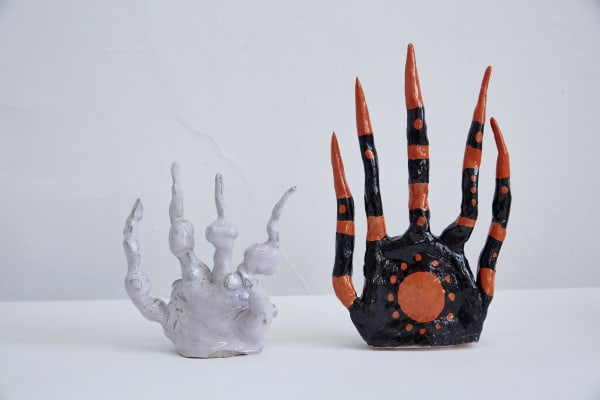 Ceramic cartoonish hands in 2 different sizes. The smaller hand has a white glaze. The larger one has a black and orange glaze. 
