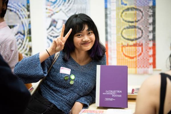 A person holding up a peace sign with their fingers next to a book 
