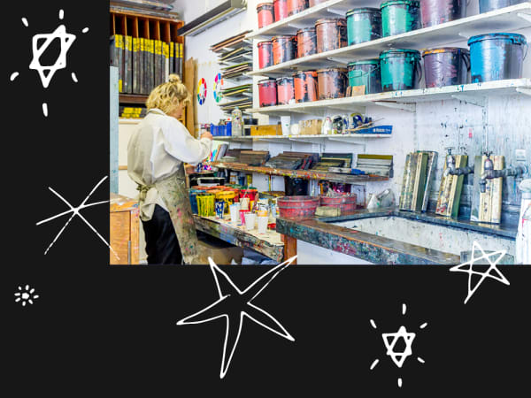 a person in a screen printing workshop, working in front of multiple shelves of paint