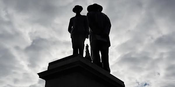 Two figures silhouetted against the sky on a plinth