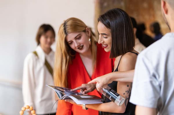 Two smiling female prospective students looking through a booklet of student work