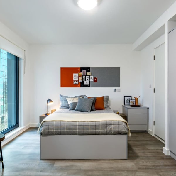 view of studio decorated in orange and grey tones showing large window, wood effect flooring, large bed and bedside table with drawers