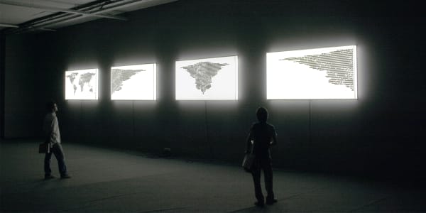People looking at an art installation of light boxes with world maps printed on them