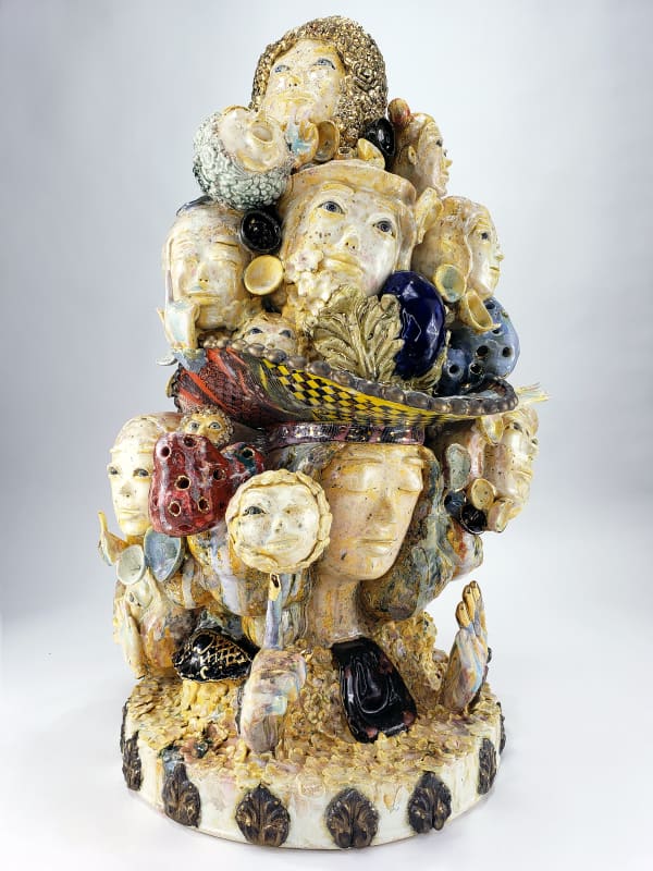 Lots of faces on a tall sculpture surrounded by mushrooms and foliage