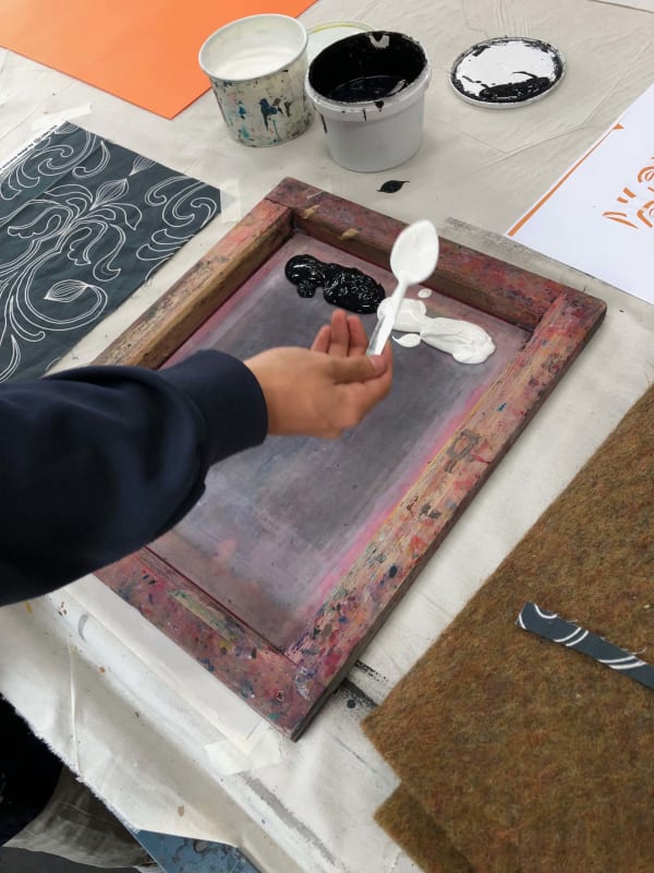 A students hand brushes white and black paint onto a canvas with a wooden frame