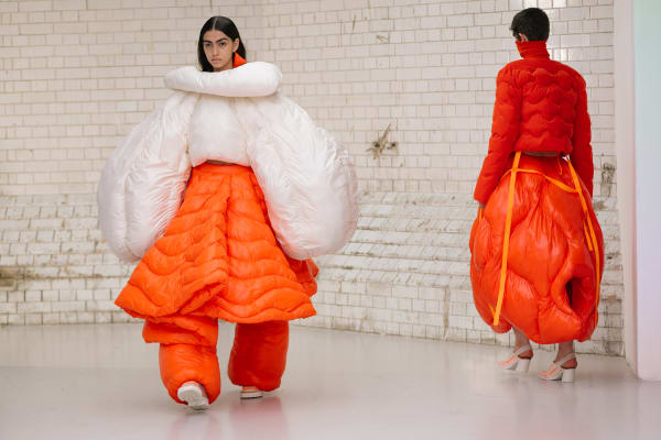 Two models walking to and from the crowd wearing orange and white inflatable outfits. 