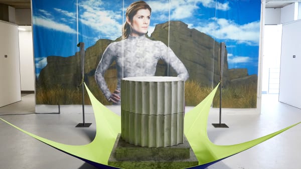 MA Fine Art installation with photographic print of a woman in front of mountains and in front of the print is a sculpture of part of a Greek column on top of a green rubber sheet
