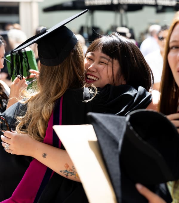 Two people hugging outside the Southbank Centre. One is wearing their graduation hat and gown.