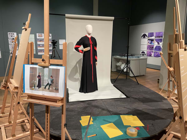 Dummy model with a dress surrounded by painting tripods and canvases.