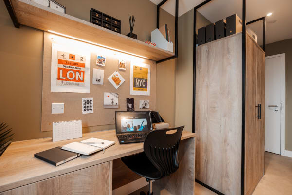 View of a bedroom desk area in the bedroom with overhead lighting, wall mounted shelf and noteboard area