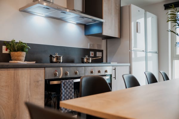 Side view of a kitchen space with a large wooden table , two cookers with extractor fans and two tall fridges 