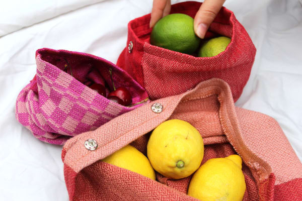 Three pink fabric woven bags one contains lemons and the other limes