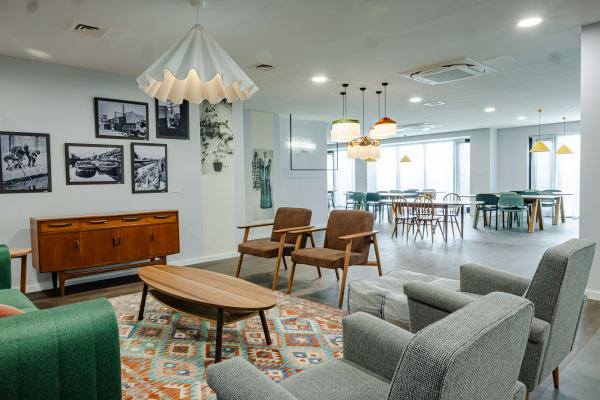 View of a large common room featuring upholstered sofas and chairs in a cozy nook, mismatched retro ceiling lampshades and a gallery wall displaying historic local images.