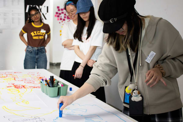 A group of people stand over a table, smiling as they draw