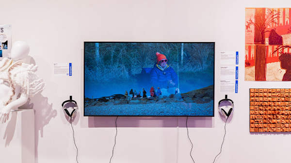 Mounted screen in a gallery showing a lady on the beach