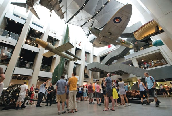 People standing underneath hanging aeroplanes in a museum.