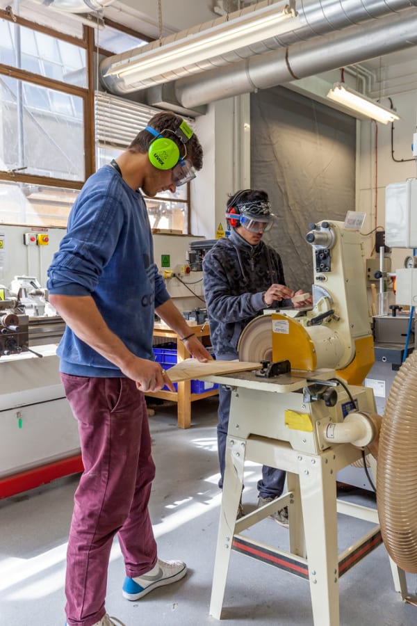 Boy in goggles and ear protection gear operating machinery in a workshop 