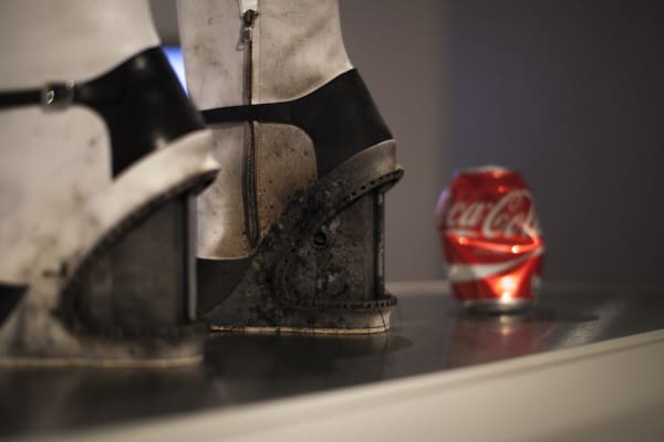 close up of scuffed black and white boot heels, beside a crushed coca-cola can.