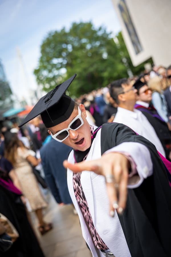 Graduate with white glasses points at camera 