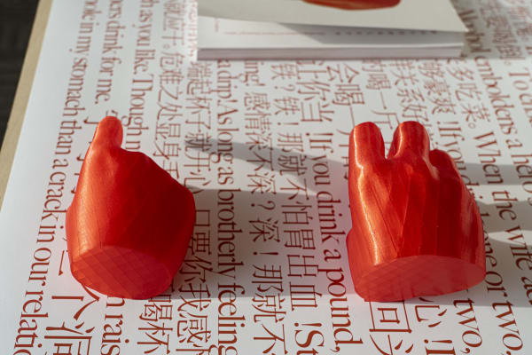 two orange hand scultures arranged on a white page with red text and characters. 