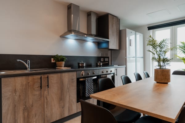 View of a kitchen space with a large wooden table , two cookers with extractor fans, sink, cabinets and two tall fridges 