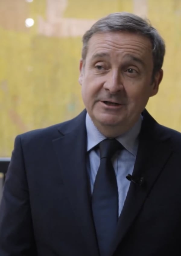 Gregor Muir in conversation. He has short, grey hair and wears a blue shirt and blue tie under a dark suit. 