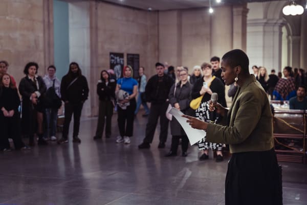 A person performing spoken word at Tate Britain, surrounded by a crowd.