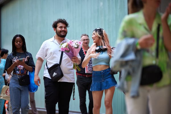 Smiling people entering the College, one is holding a bunch of flowers