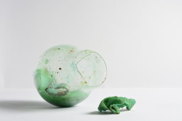 A smashed glass lightbulb with green oxidised crystals growing out of it