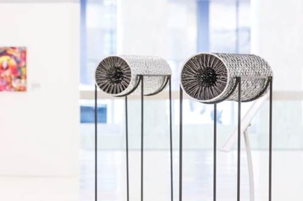 Two circular tubes covered in sequins, on stands in a gallery space