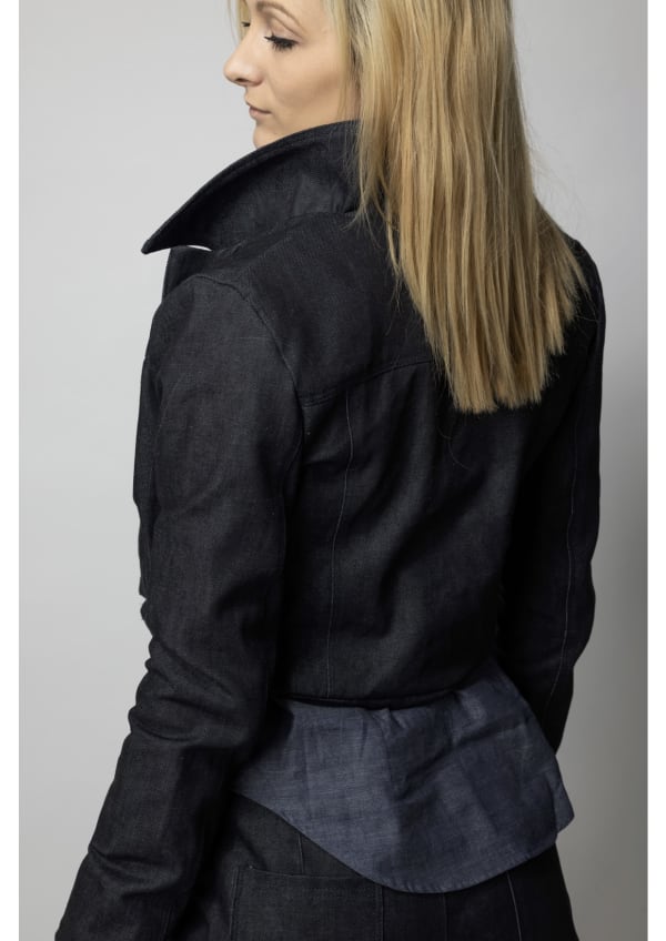 Photo of a woman wearing a denim jacket and jeans. She has her back to the camera and is looking over her shoulder
